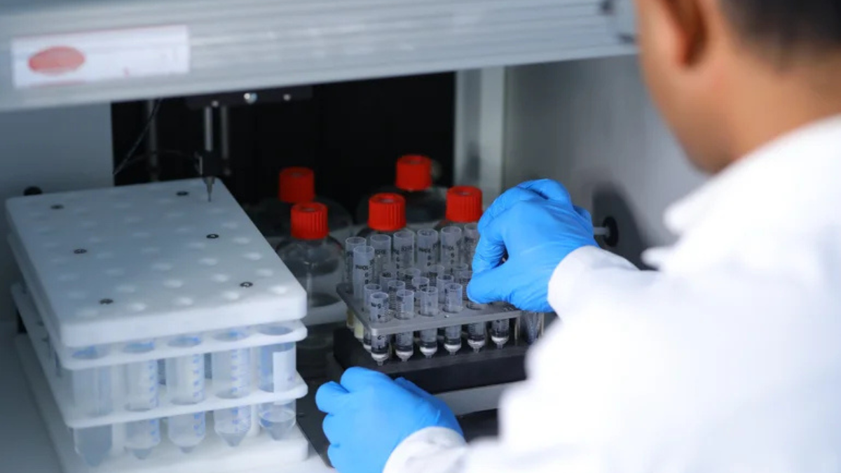 Gloved hands loading test tubes into automated lab equipment.