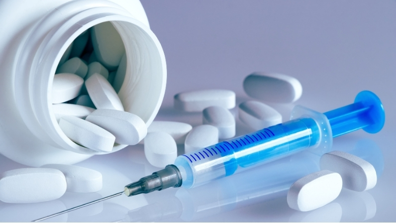 Pills and syringe representing competing cholesterol drug delivery methods