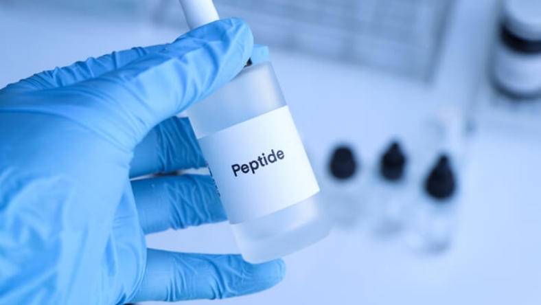 Laboratory vial marked peptide held by researcher in blue gloves